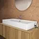 Waschtisch von Ideal Standard, rechteckig in Weiß, montiert auf einer Holzablage, mit einem modernen Wasserhahn und runder Spiegelfläche an der Wand.